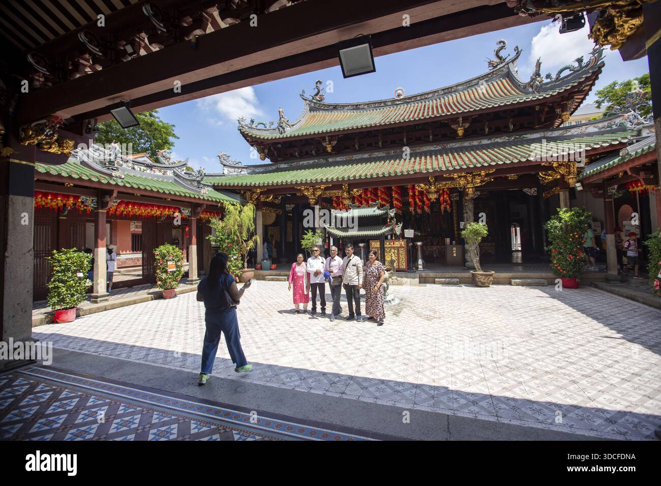 Singapore, Singapore - 14 maggio 2024: Vista del tetto ornato del tempio Thian Hock Keng contro un cielo luminoso, che incornicia un gruppo di visitatori nel cortile. Foto Stock