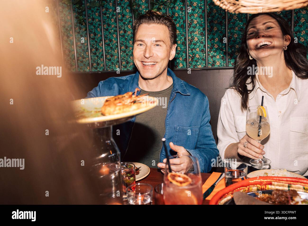Uomo felice che passa il piatto ad un amico mentre cena e beve al ristorante Foto Stock