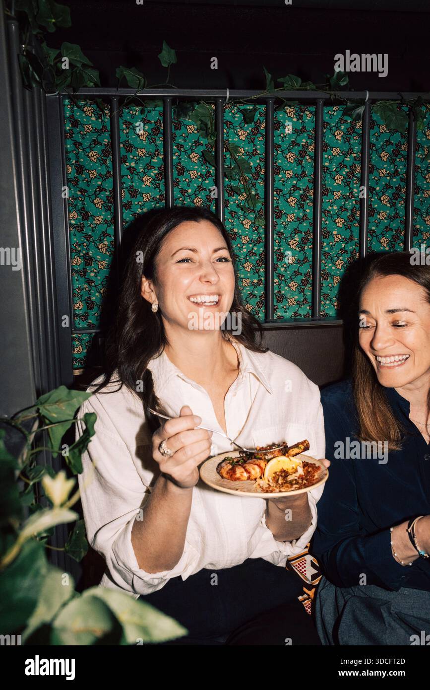 Donna felice che mangia gamberi seduto con un'amica al ristorante Foto Stock