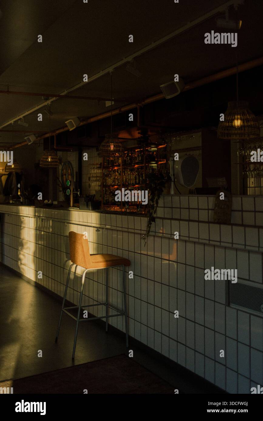 La luce del sole che cade sulla sedia tenuta vicino al bancone del bar piastrellato nel ristorante vuoto Foto Stock