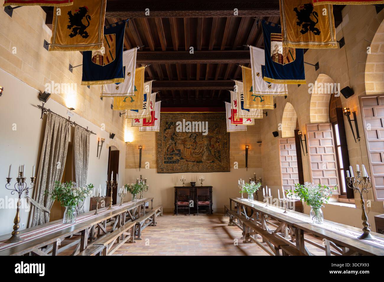 Almodoval del Rio, Spagna - 21 maggio 23: Una grande sala con travi in legno, decorata con bandiere e un grande arazzo, con lunghi tavoli e cent floreali Foto Stock