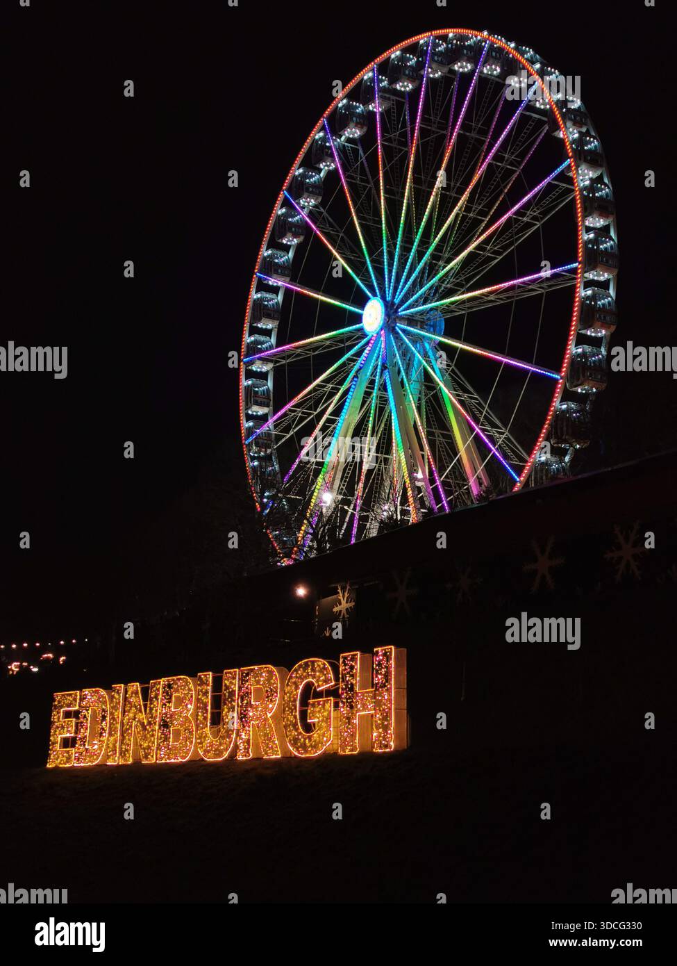 Scene festive dal mercato di Natale di Edimburgo con bancarelle luminose, edifici illuminati e un gigantesco cartello illuminato di Edimburgo che creano una scena vivace. - Immagine stock catturata con smartphone