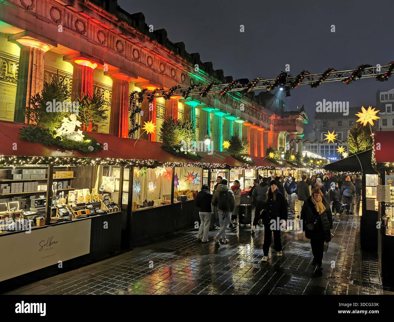 Scene festive dal mercato di Natale di Edimburgo con bancarelle luminose, edifici illuminati e un gigantesco cartello illuminato di Edimburgo che creano una scena vivace. - Immagine stock catturata con smartphone