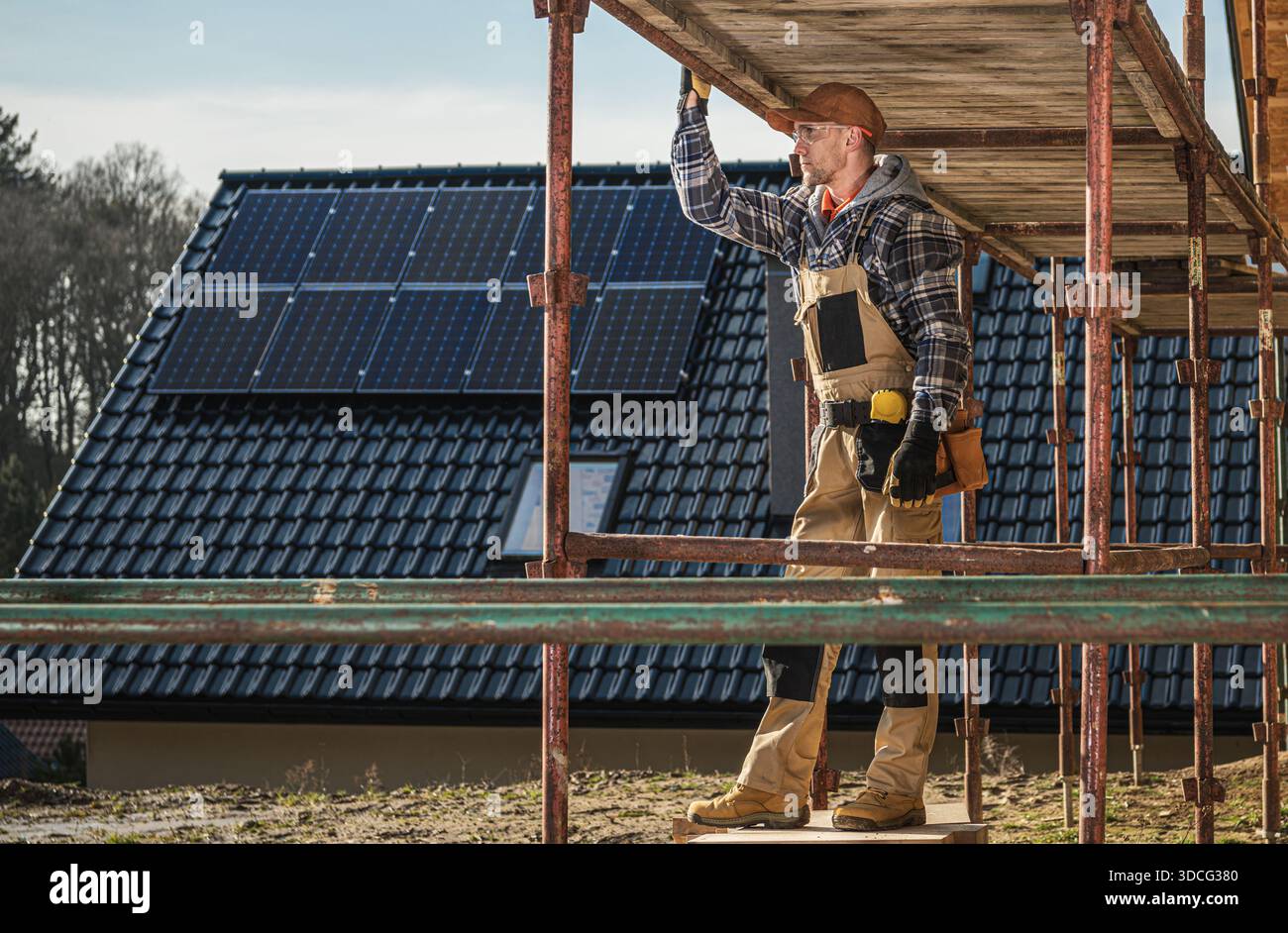 L'operaio edile sta allestendo ponteggi in un cantiere con pannelli solari sul tetto. Foto Stock