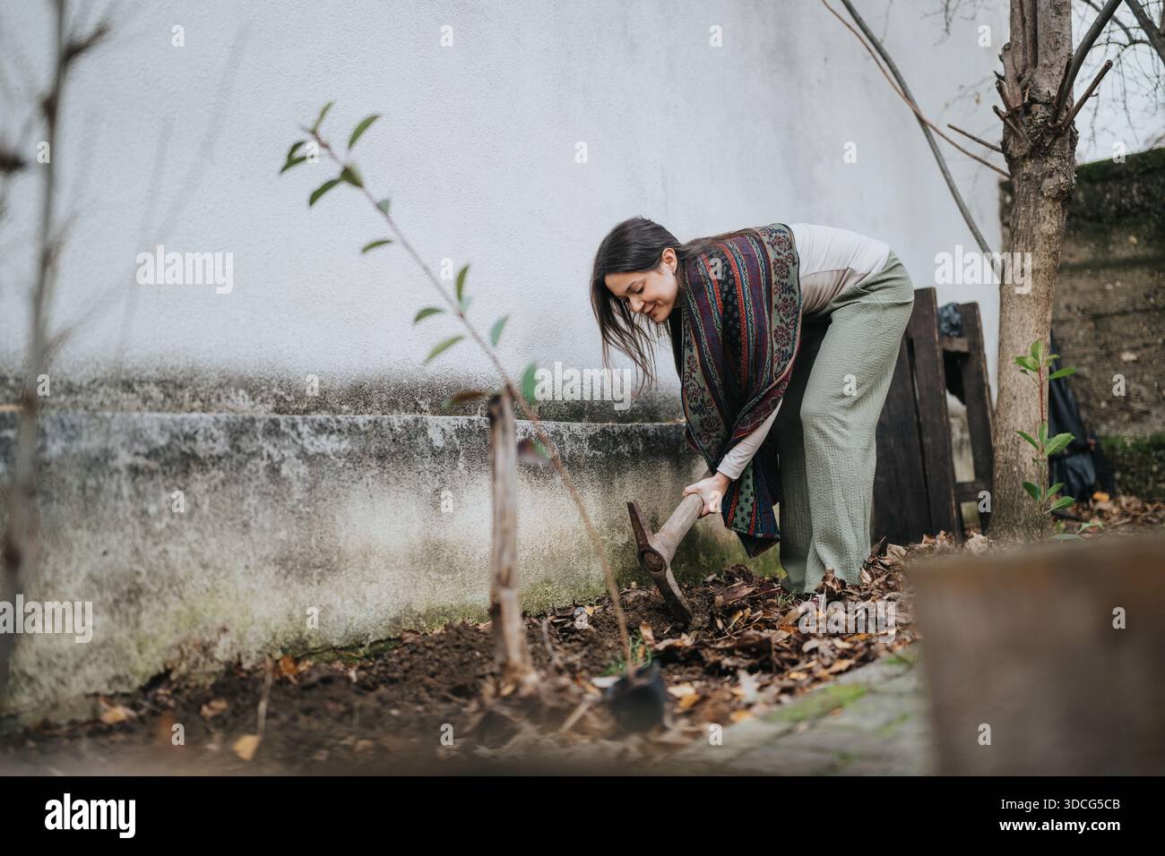 Donna giardiniera che scavava in un piccolo giardino accanto a un muro con una sciarpa a motivi geometrici oggi Foto Stock