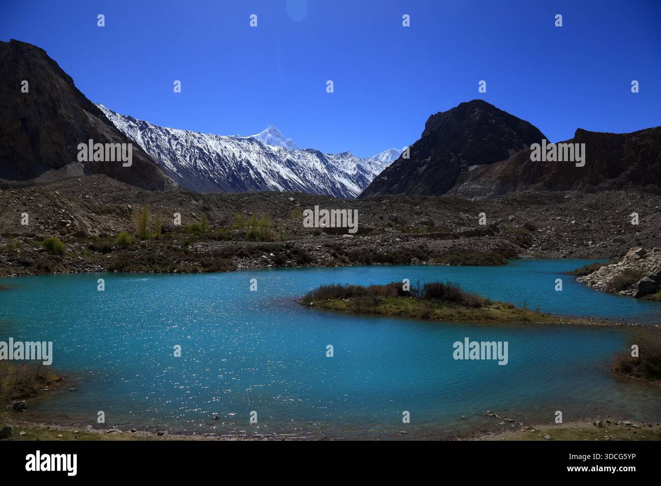 Vista di un lago glaciale turchese che rispecchia il forte contrasto di aspre montagne innevate sotto un cielo limpido, creando una terra serena ma suggestiva Foto Stock