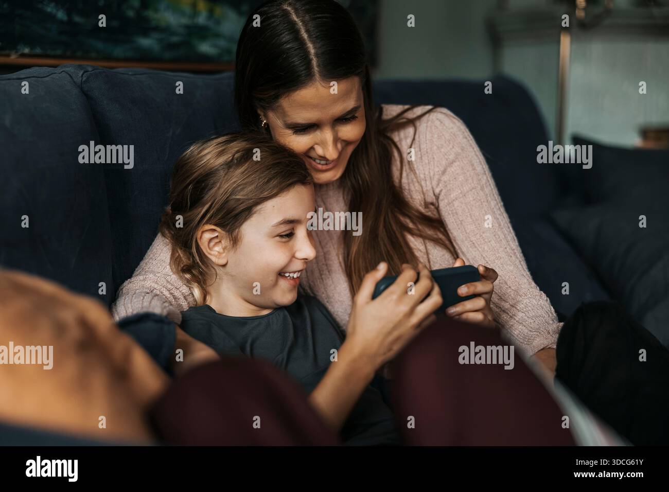 Mamma e figlia sorridenti che trascorrono il tempo libero guardando video sullo smartphone a casa Foto Stock