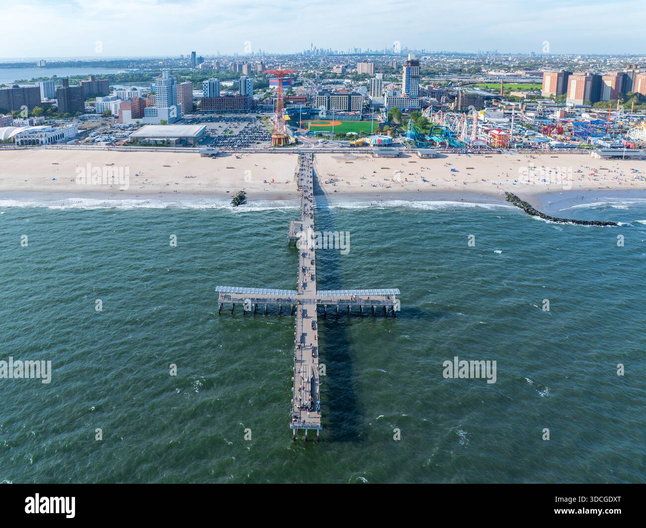 Vista aerea di un molo che si estende nell'oceano, in contrasto con il paesaggio urbano, tra cui l'iconica ruota panoramica e il vivace divertimento di Coney Island Foto Stock