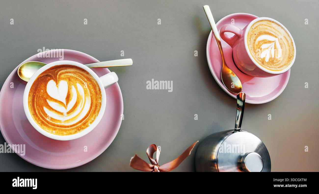 Due tazze di cappuccino con latte art a forma di fiore su piattini rosa su un tavolo. Vista dall'alto Foto Stock