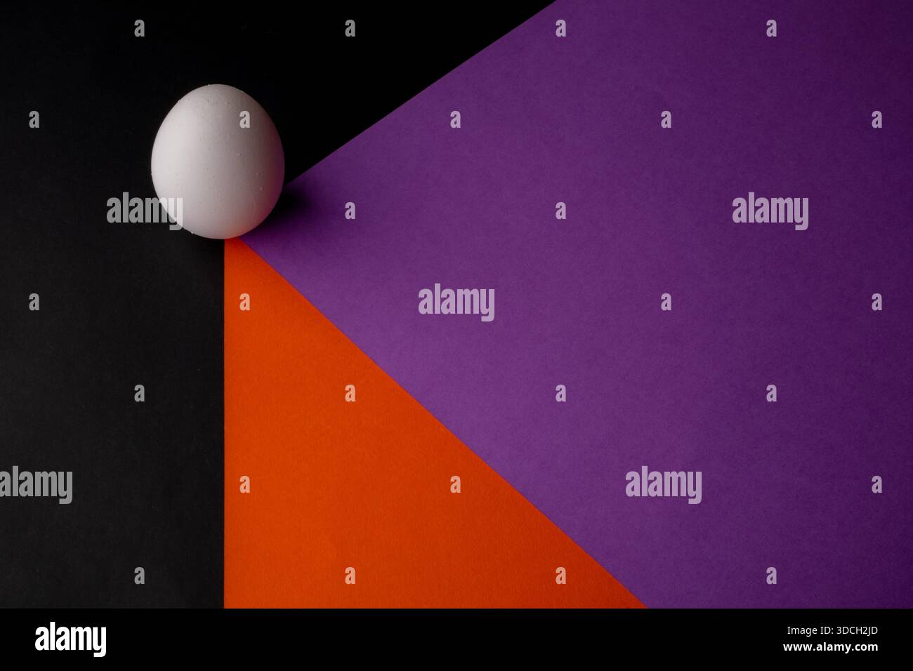 Uovo bianco su sfondo geometrico colorato con sezioni nere, viola e arancioni. Foto Stock