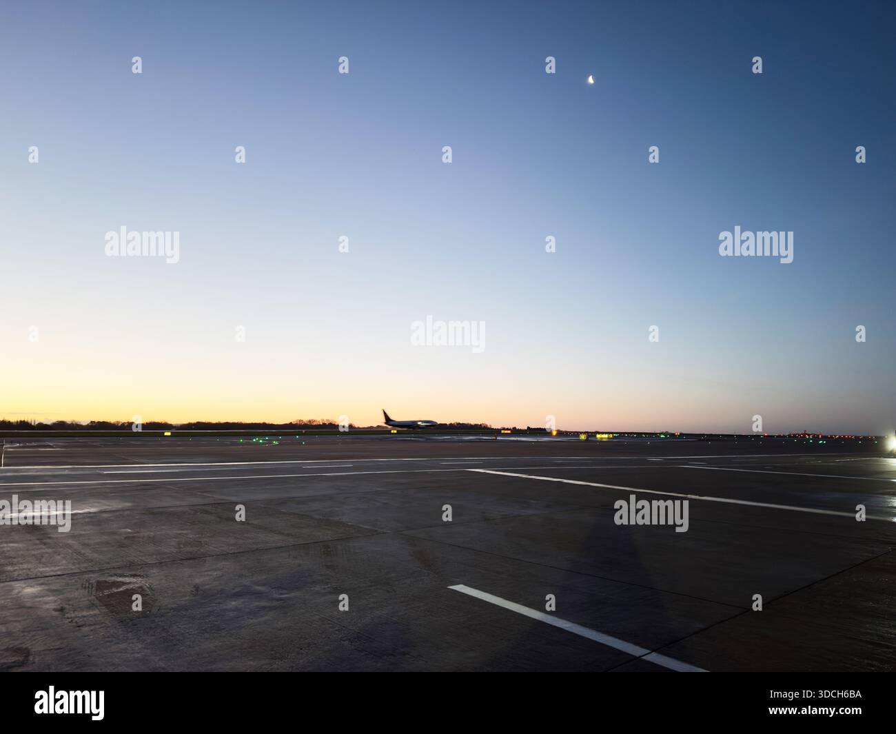 Manchester, Regno Unito - 13 dicembre 2025: Un'alba serena all'aeroporto di Manchester, aereo sulla pista sotto una pallida luna crescente. Foto Stock