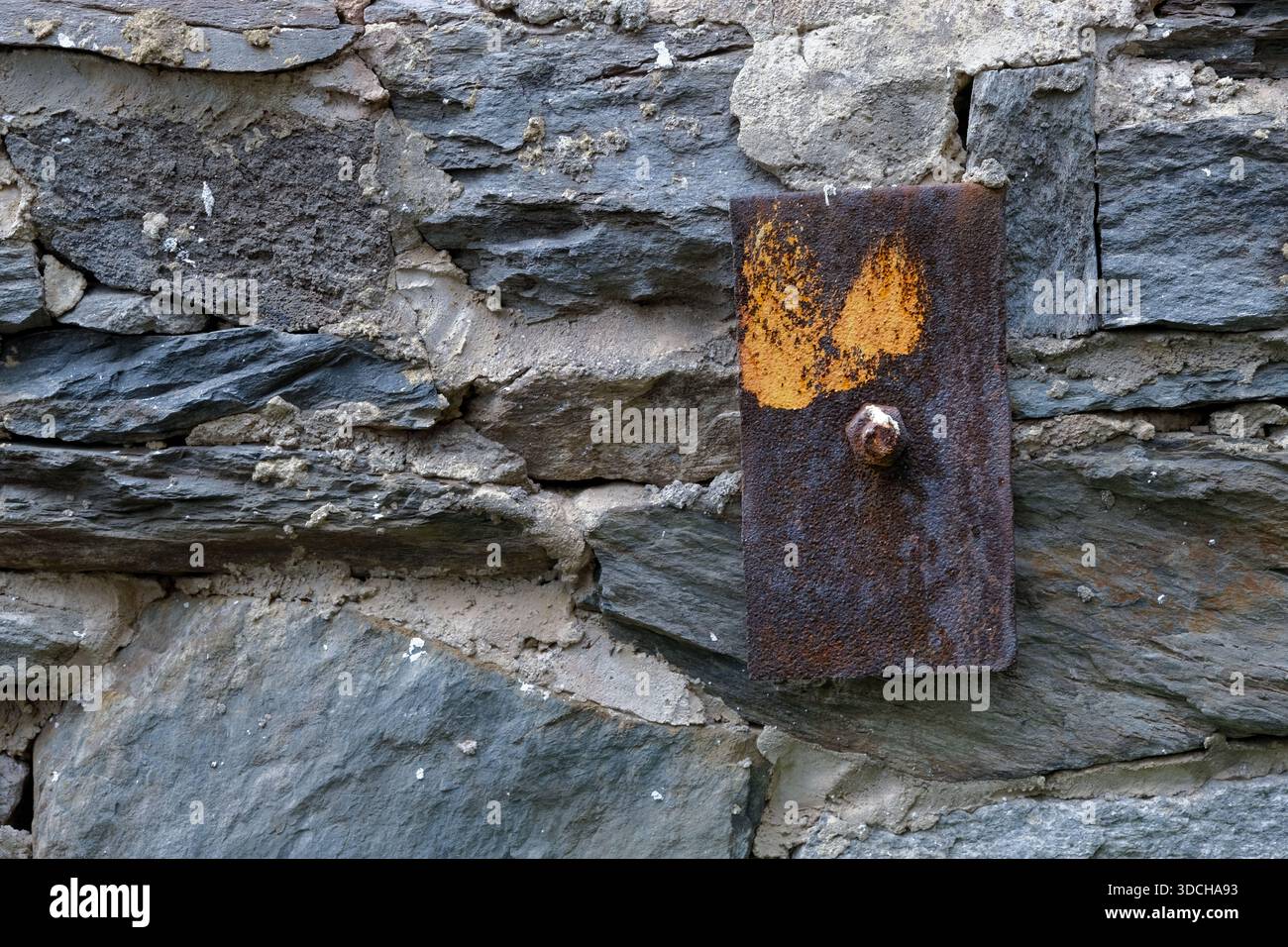 Vecchia parete in pietra e tassello in metallo arrugginito Foto Stock