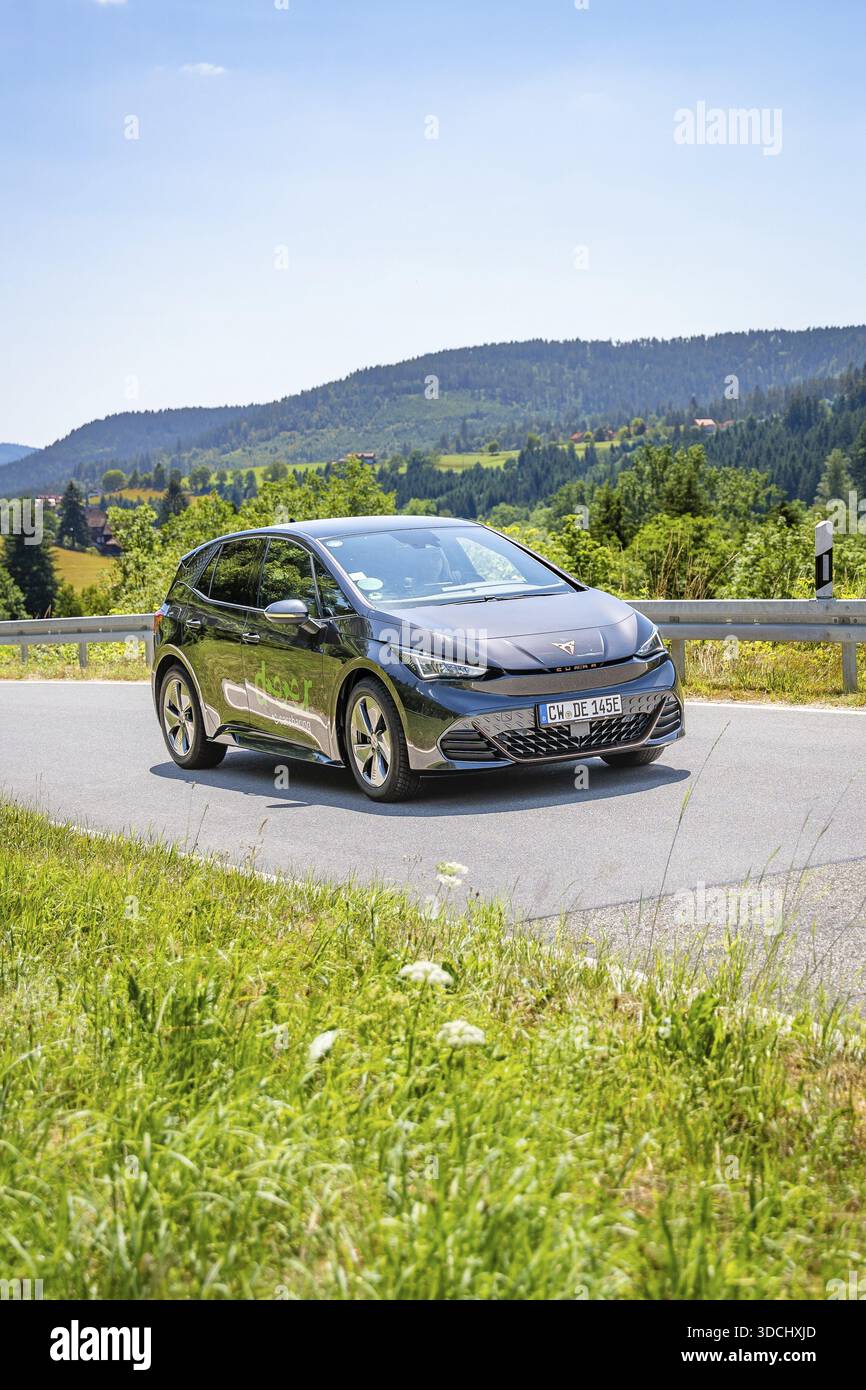 Auto nera che guida su una strada attraverso un paesaggio collinare alla luce del giorno, condivisione di e-car con cervi, auto elettrica Cupra, Germania Foto Stock