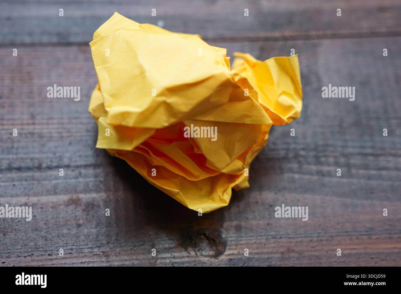 Un pezzo di carta gialla leggermente stropicciato posto su una superficie di legno scuro con motivi a grana visibili. Foto Stock