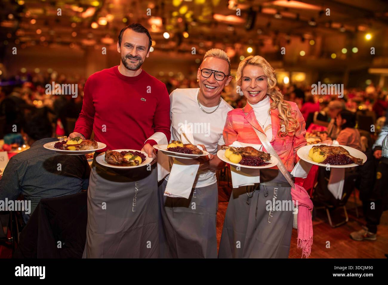 abb: David Biethig, Sascha Lauterbach und Victoria Herrmann als Promi Kellner beim Servieren von Teller mit Gaensekeuele Rotkohl und Kloesse bei der 31. Frank Zander Weihnachtsfeier Weihnachtsessen fuer Obdachlose und Beduerftige Menschen 2025 im Estrel Convention Center AM 22.12.2025 a Berlin Berlin Berlin Deutschland Foto Stock