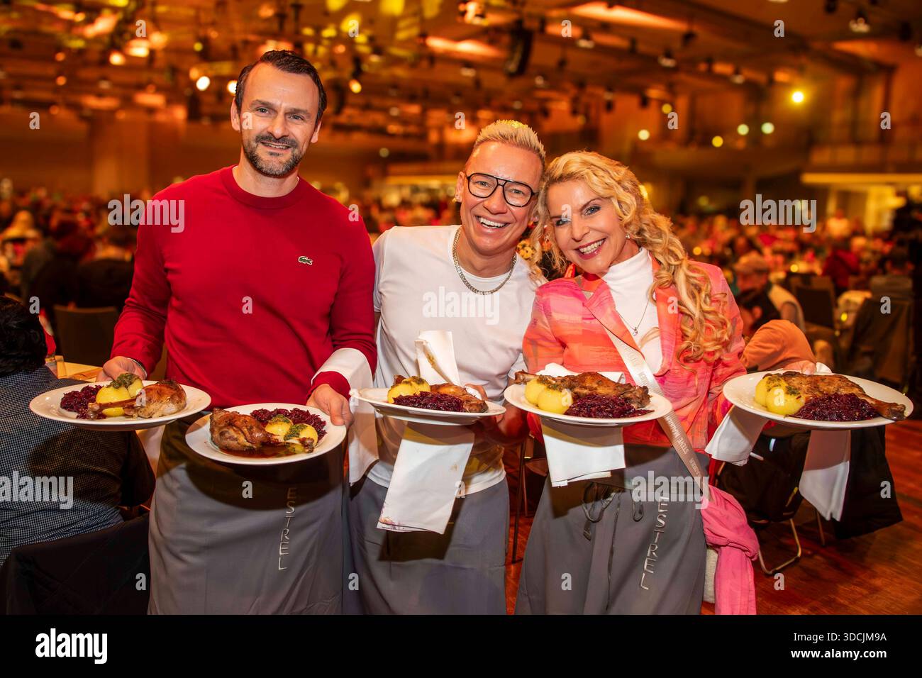 abb: David Biethig, Sascha Lauterbach und Victoria Herrmann als Promi Kellner beim Servieren von Teller mit Gaensekeuele Rotkohl und Kloesse bei der 31. Frank Zander Weihnachtsfeier Weihnachtsessen fuer Obdachlose und Beduerftige Menschen 2025 im Estrel Convention Center AM 22.12.2025 a Berlin Berlin Berlin Deutschland Foto Stock
