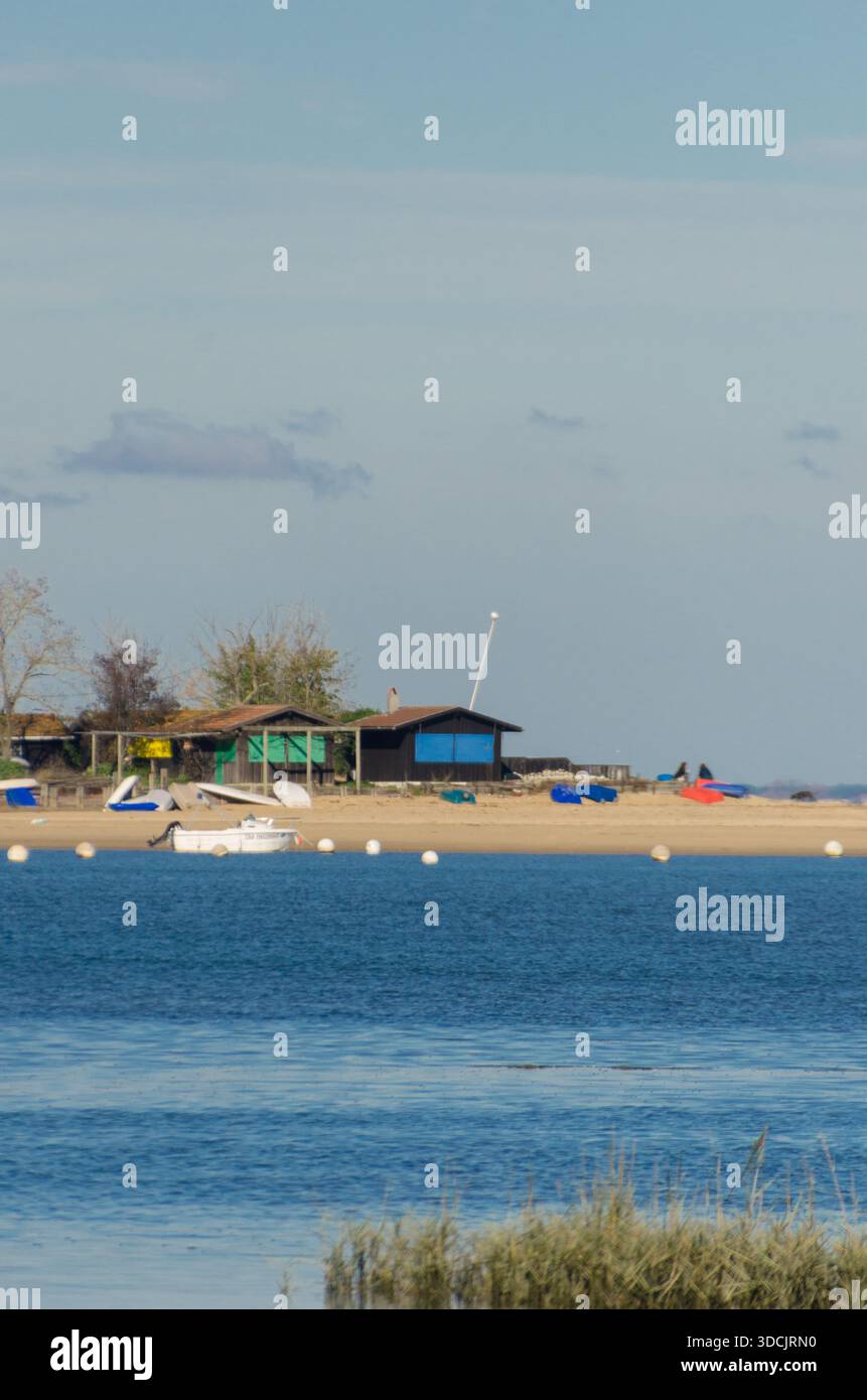 Vista di una costa tranquilla con baracche di legno annidate sulla spiaggia sabbiosa, dove riposano le barche e la tranquilla acqua blu incontra la riva, Arcachon, Fran Foto Stock