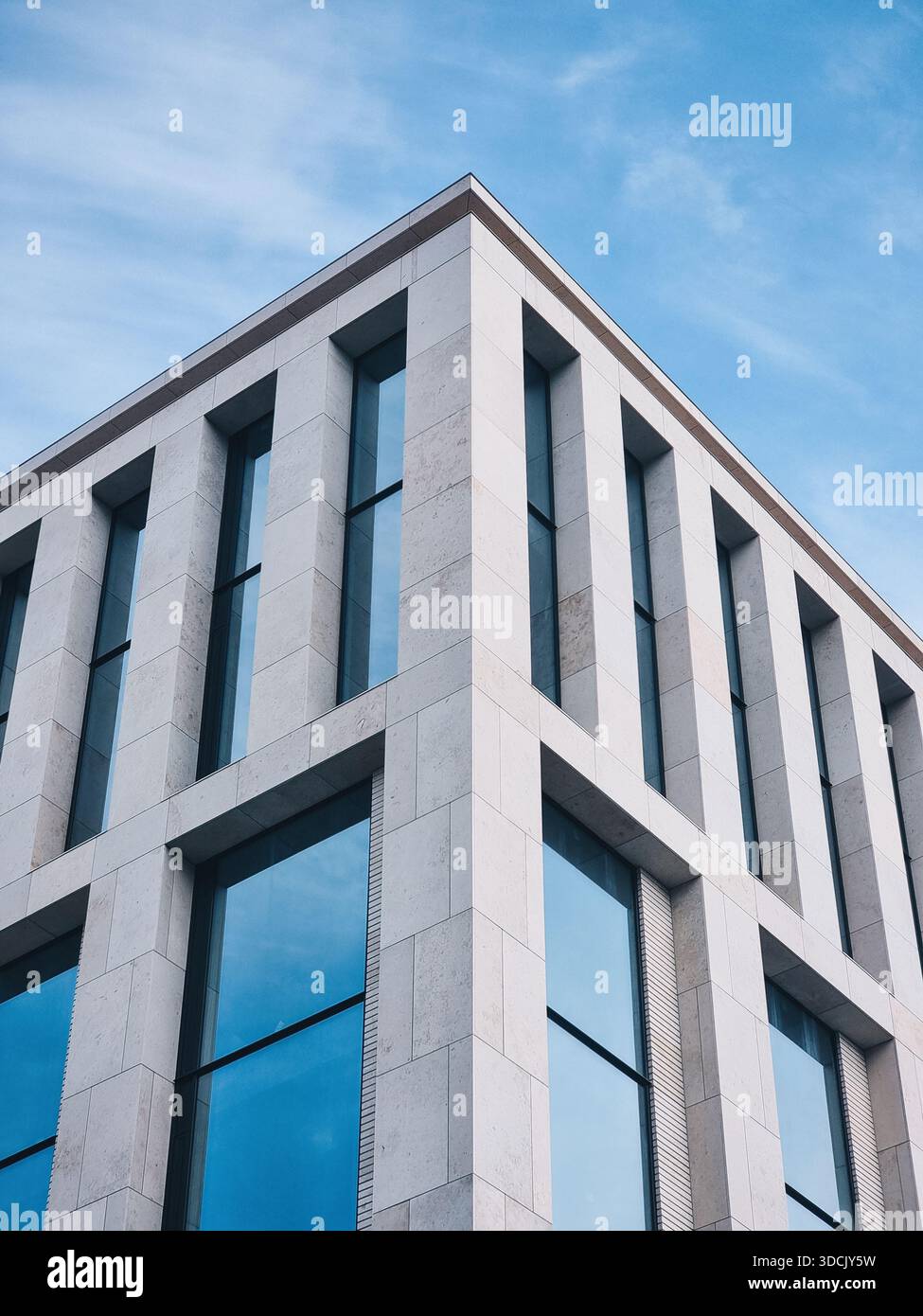 Affacciandosi sulla facciata di un edificio moderno con facciata in piastrelle di pietra. Angolo di elegante edificio residenziale con alte finestre; giorno di sole, cielo blu. Foto Stock