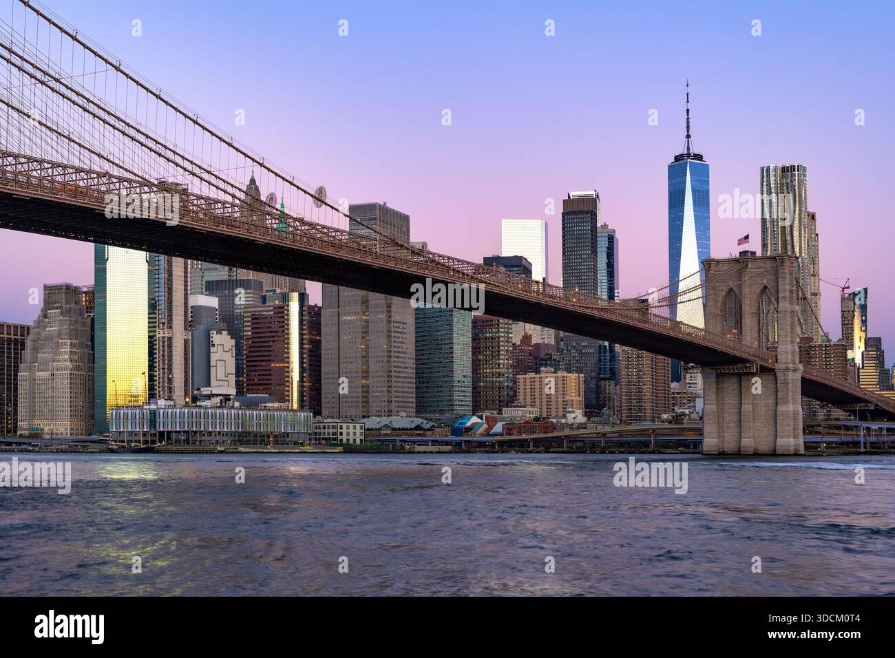 L'iconico ponte di Brooklyn si estende sull'East River e conduce allo skyline di Lower Manhattan durante una tranquilla alba viola. Foto Stock