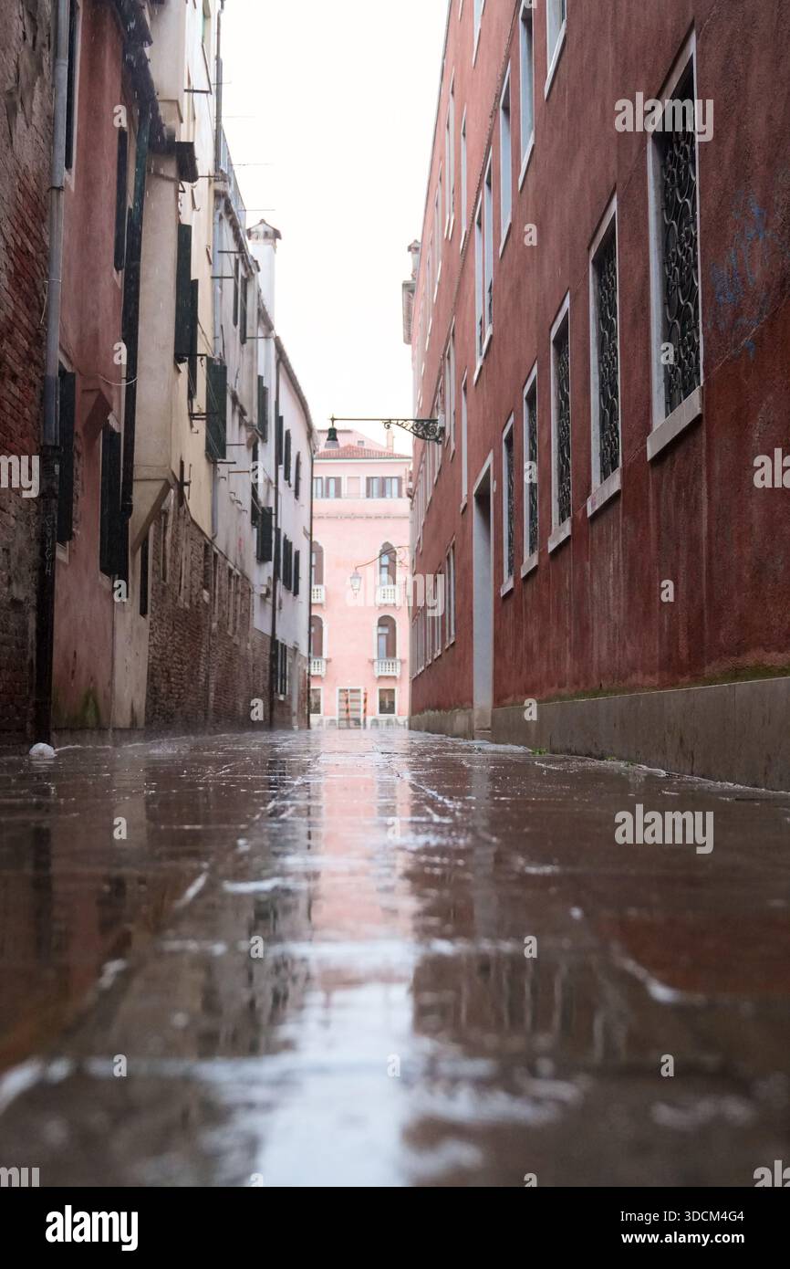 Viaggia nel vicolo italia venezia e venezia con il pavimento bagnato che riflette i vecchi edifici colorati sotto un cielo luminoso Foto Stock