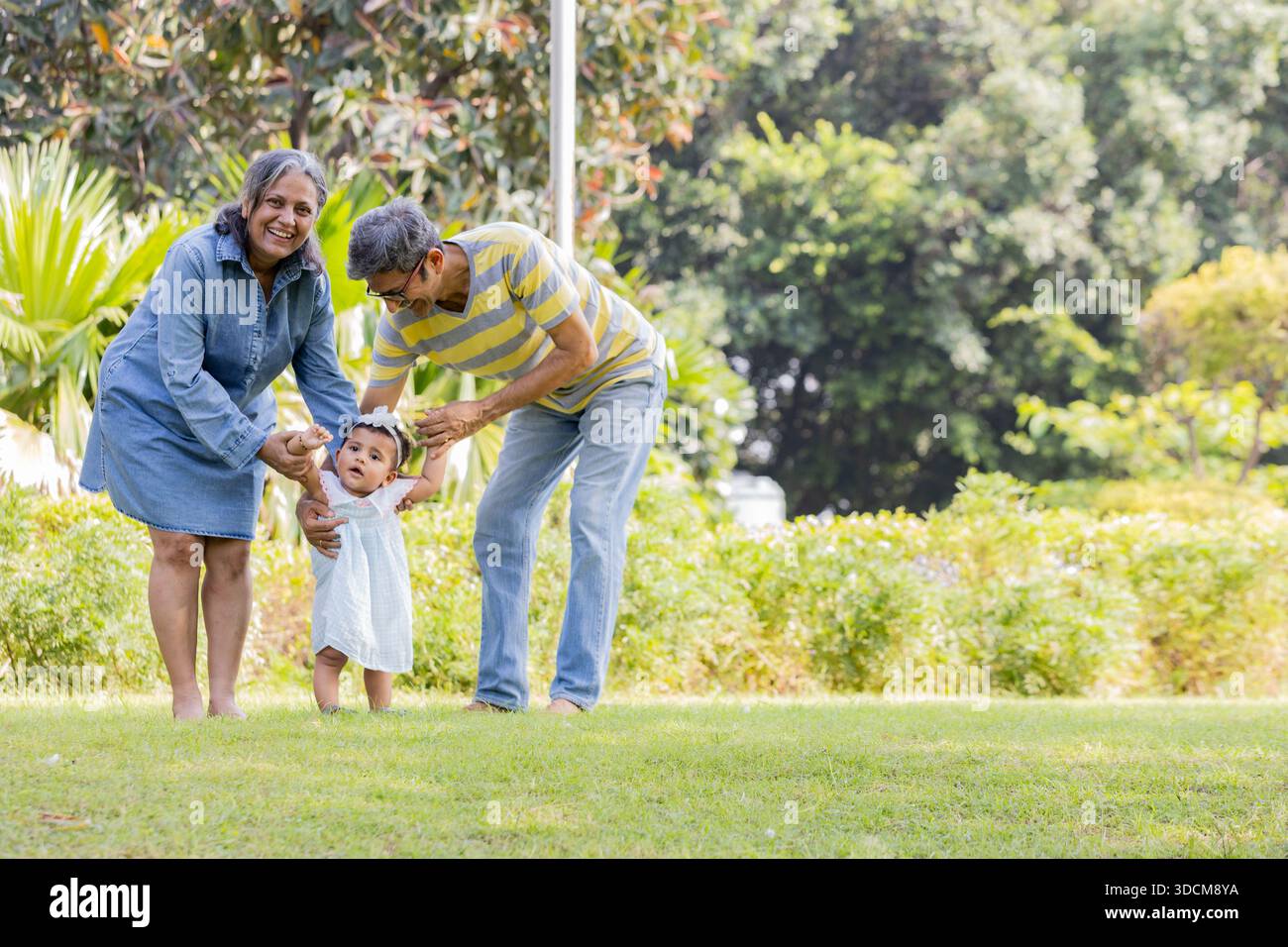 Coppia di anziani indiani che sostiene il nipote imparando a camminare all'aperto Foto Stock