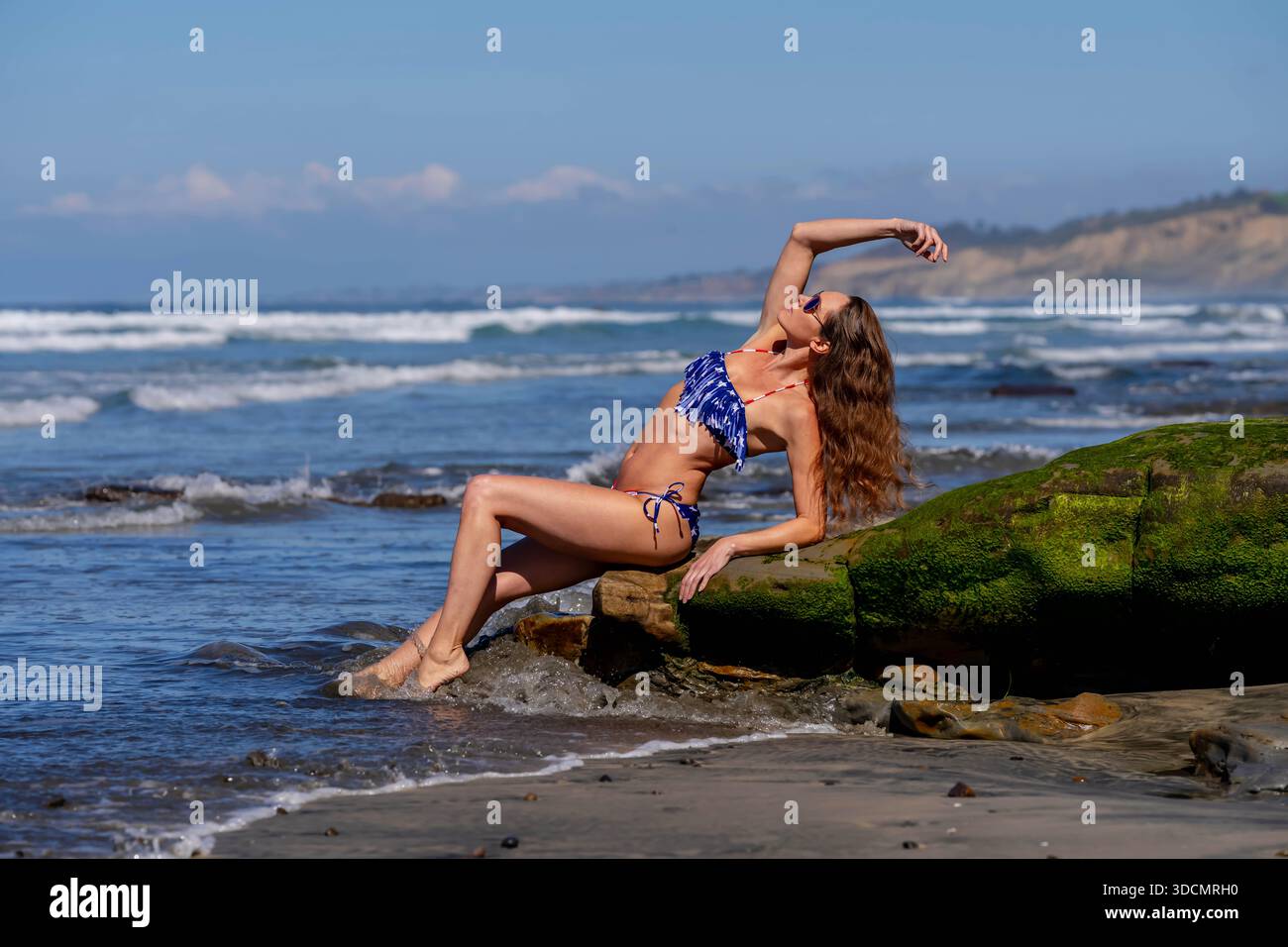 Una donna mozzafiato si crogiola nella beatitudine della spiaggia, vicino a un molo, sotto cieli azzurri, abbracciando la serenità di una giornata perfetta in riva al mare Foto Stock