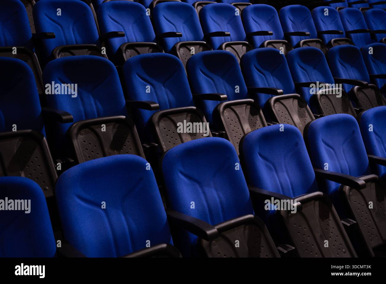 File di sedie blu vuote che offrono posti a sedere in un moderno auditorium, cinema o sala conferenze con accenti scuri Foto Stock