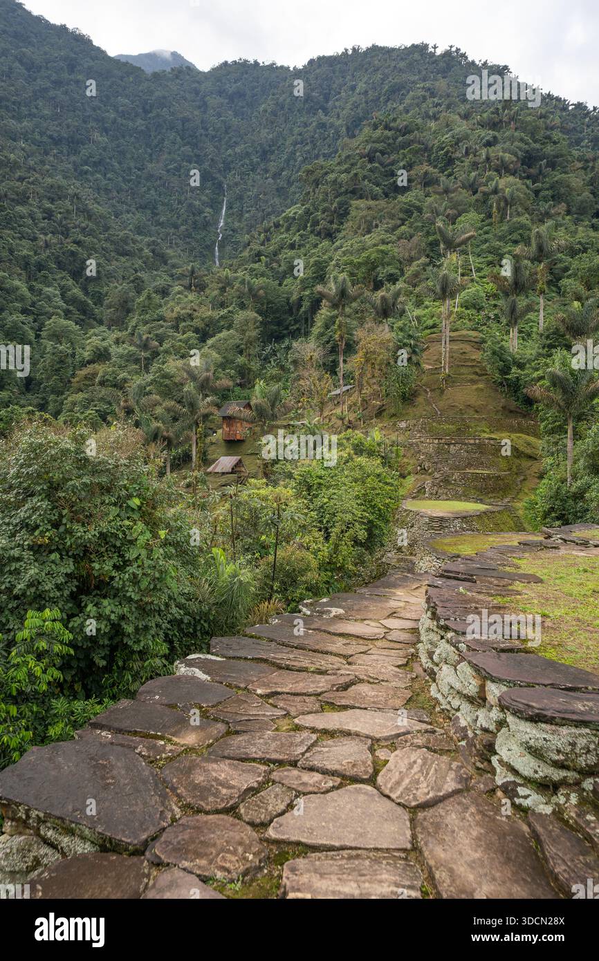 Una vista verticale ad alto angolo di un sentiero asfaltato in pietra che conduce attraverso le rovine, oltre antiche terrazze circolari e rustiche capanne in legno, surroun Foto Stock
