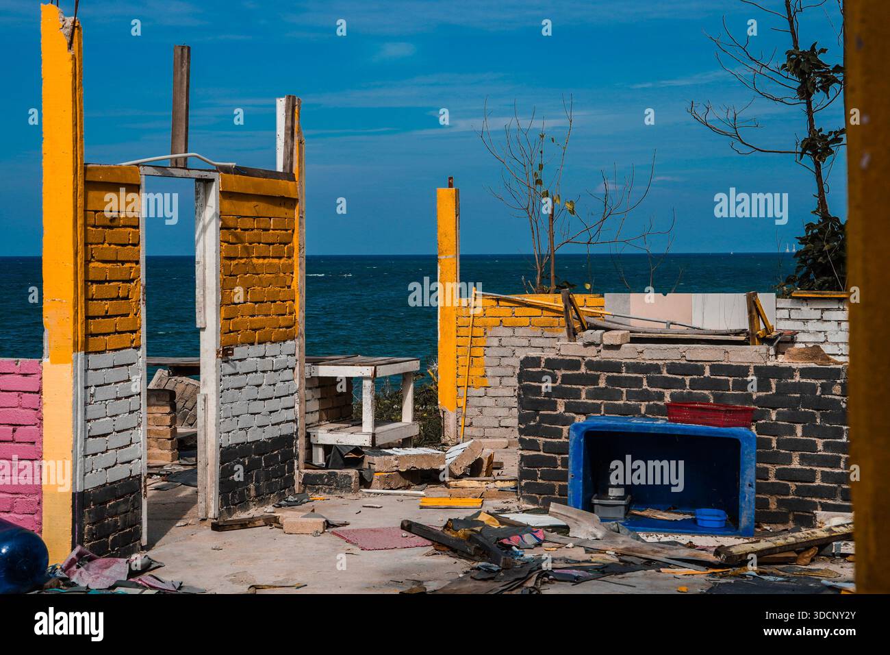 resti sbriciolati di una struttura in mattoni demolita contro un oceano blu profondo e un cielo luminoso. Foto Stock