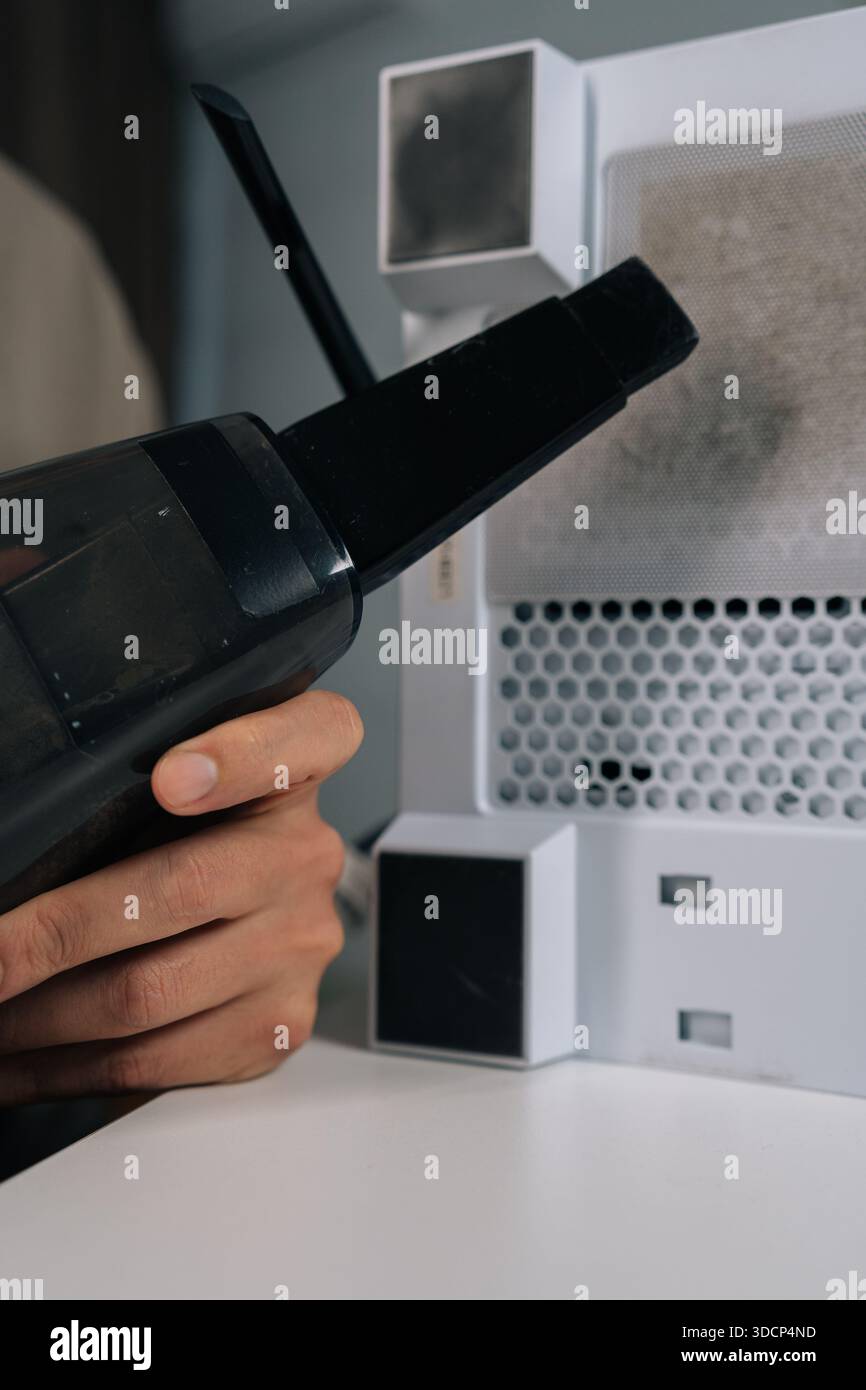 Colpo ritagliato verticale del riparatore che aspira la polvere dal filtro di scarico del pc desktop e dal pannello a rete durante la manutenzione ordinaria dell'unità di sistema per evitare che ciò accada Foto Stock