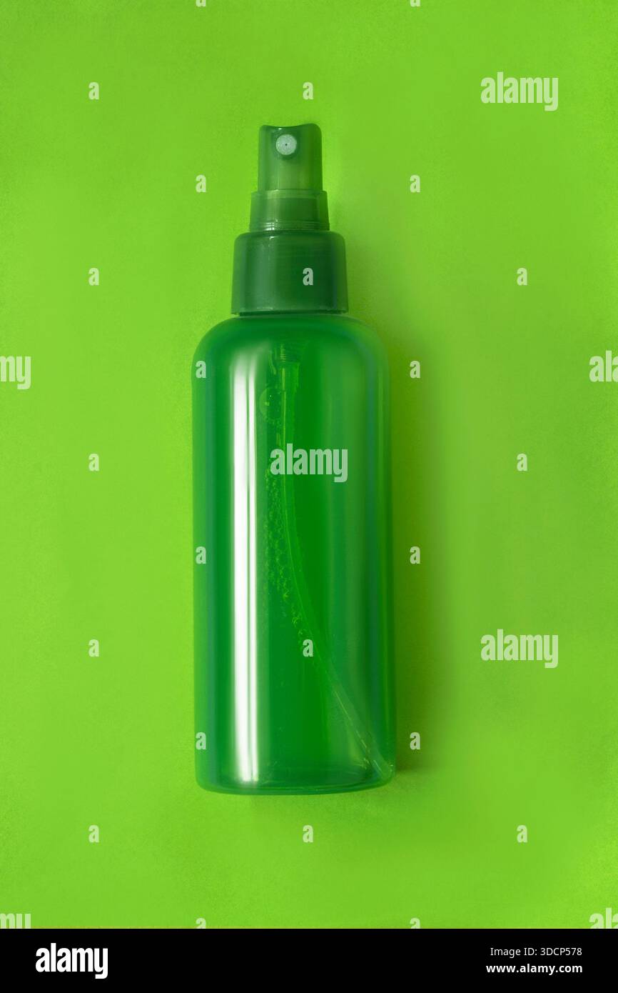 Prodotto cosmetico verde che spruzza la bottiglia su sfondo verde neon studio Foto Stock