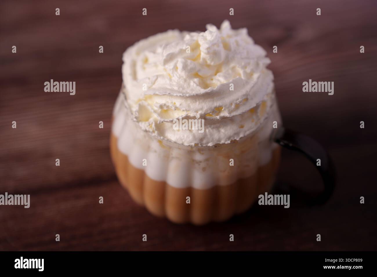 primo piano di una bevanda a strati di caffè in una tazza di vetro condita con abbondante panna montata su una superficie di legno che evoca un'atmosfera intima e appagante con sof Foto Stock