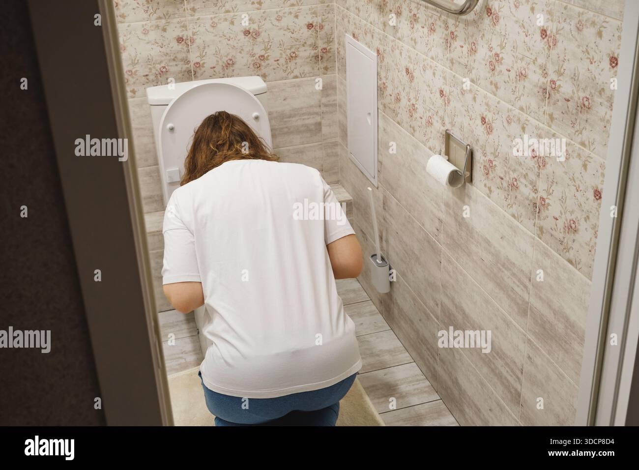 La giovane donna si sente male e soffre di nausea, appoggiata sulla ciotola del gabinetto Foto Stock