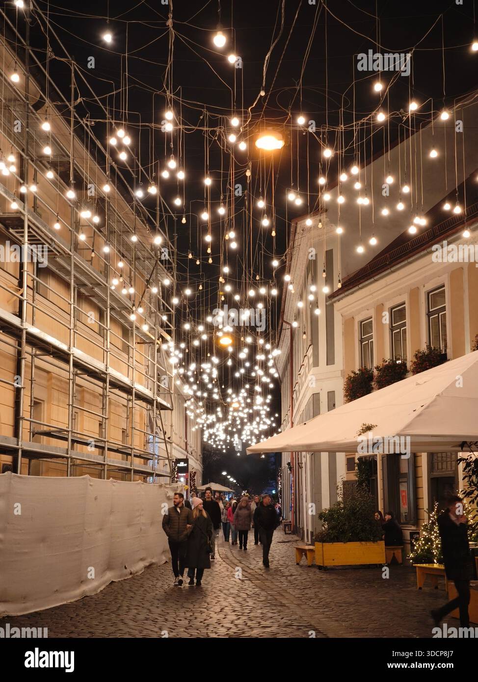 Strada notturna della città con luci festose, gente che cammina su ciottoli, bagliore caldo, atmosfera urbana accogliente, atmosfera da vacanza Foto Stock