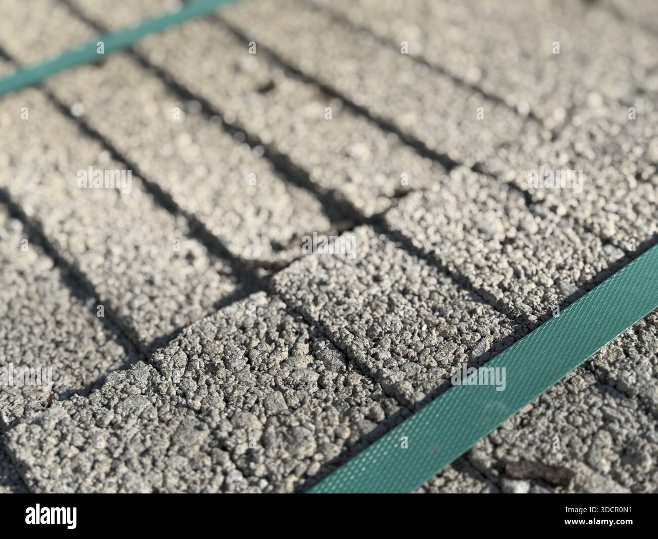 Vista ravvicinata della pavimentazione in mattoni di pietra con strisce verdi diagonali sullo sfondo luminoso della luce solare. Foto mobile Foto Stock