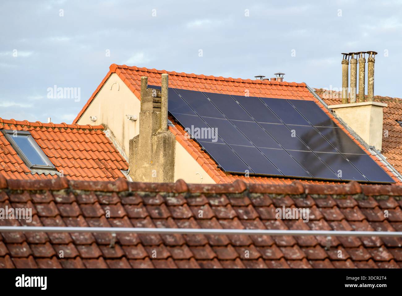 Un tetto con pannelli solari installati, circondato da tradizionali tetti e camini di tegole rosse Foto Stock