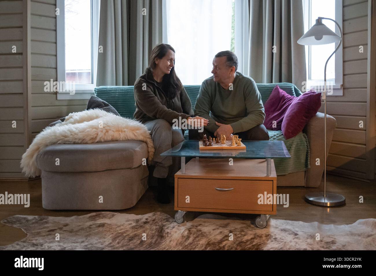 Una coppia matura seduto sul divano a casa e trascorrendo del tempo insieme giocando a scacchi, parlando e rilassandosi nell'accogliente interno del soggiorno. Home attività ricreative Foto Stock