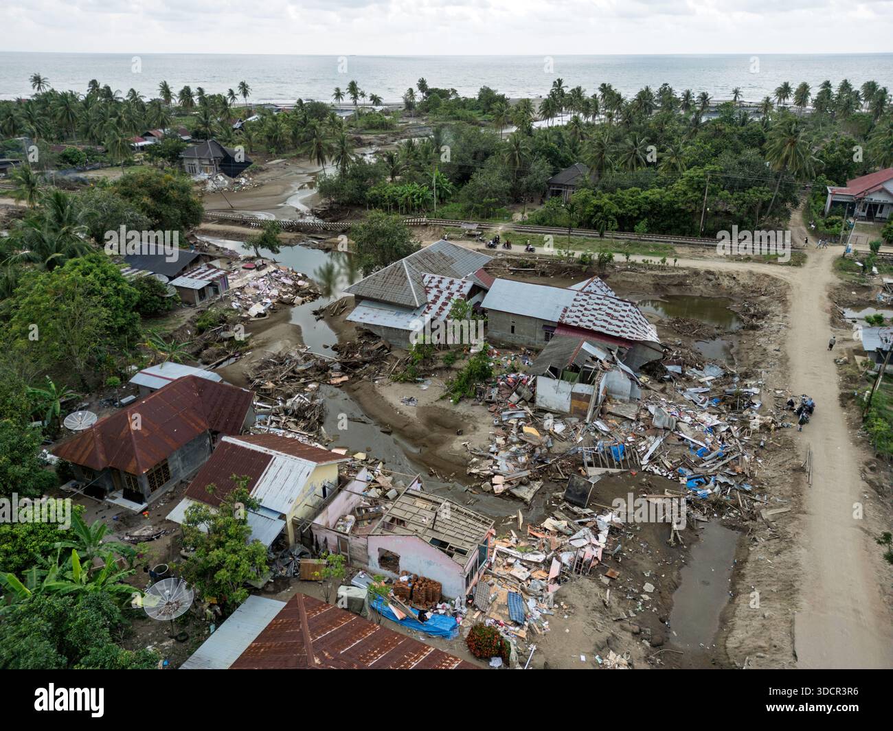 North Aceh, Indonesia. 24 dicembre 2025. Una vista aerea rivela una catastrofica erosione del suolo che ha trasformato un'area residenziale in un canale simile a un fiume nel villaggio costiero di Keude Bungkaih, nel distretto di Muara Batu. La massiccia forza dei torrenti ha spazzato via strati profondi di terreno, lasciando i binari ferroviari sospesi a mezz'aria e distruggendo le case che un tempo sorgevano sulla terra. Il paesaggio rimane pesantemente alterato un mese dopo che le massicce inondazioni hanno colpito Aceh, Sumatra settentrionale e Sumatra occidentale nel novembre 2025. Crediti: Irfan M Nur/Alamy Live News Foto Stock
