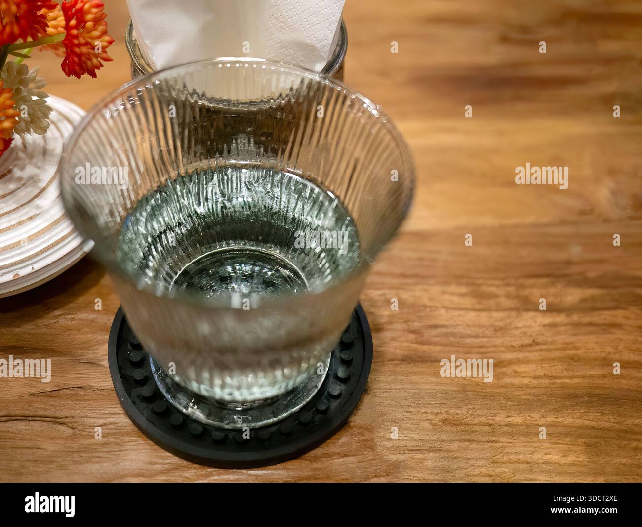 Un bicchiere di acqua potabile fresca e limpida servito in un elegante bicchierino scanalato o scanalato. La bevanda trasmette purezza, idratazione e un'atmosfera accogliente, Foto Stock