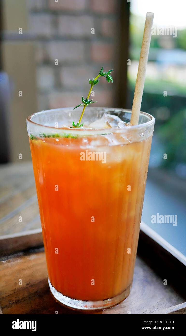 Un rinfrescante bicchiere di tè al limone ghiacciato o di tè alla pesca servito su un tavolo di legno in un bar. La bevanda color ambra è guarnita con lim verde fresco Foto Stock
