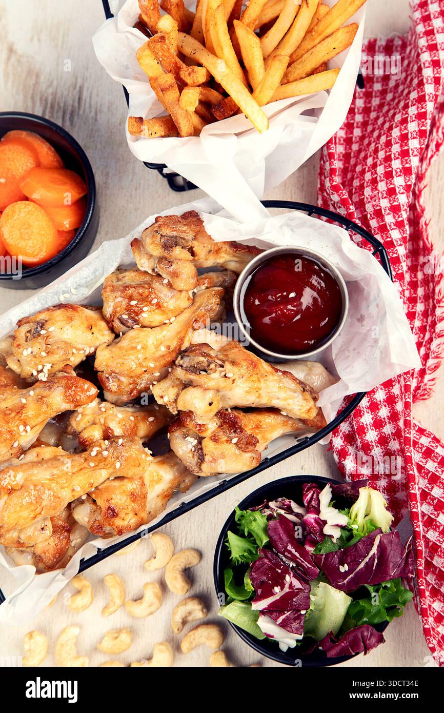 Ali di pollo fritte con salsa, patatine fritte e insalata su uno sfondo chiaro. Fast food. Vista dall'alto. Foto Stock