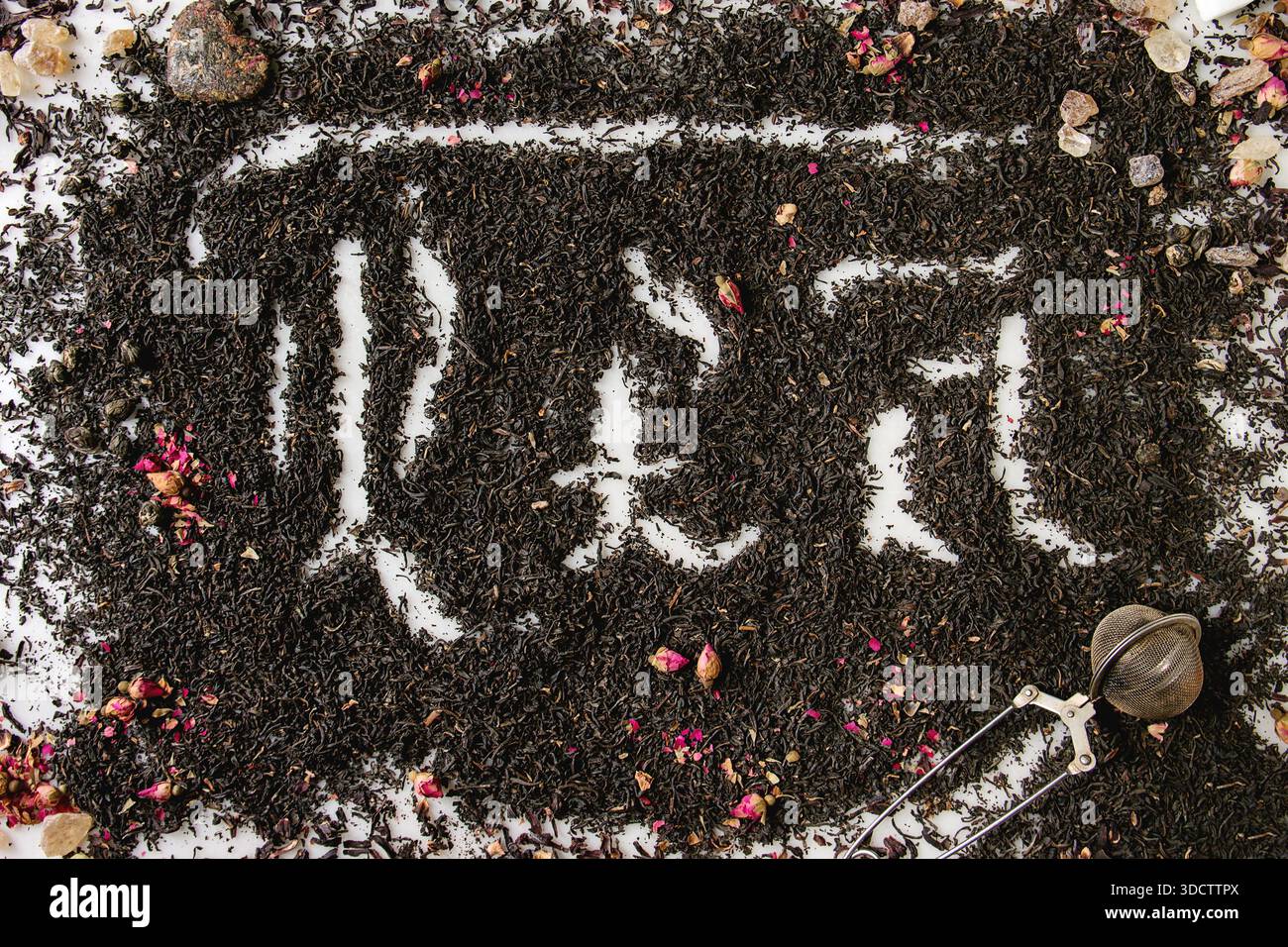 Iscrizione calligrafica lettere gotiche tè su ceylon nero secco e tè verde sparsi su marmo bianco con boccioli di rosa e colorante. Concetto di Tea drinking background. Vista dall'alto Foto Stock