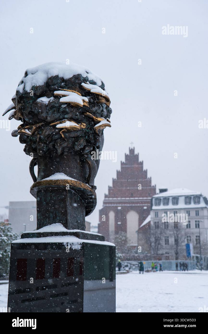 Una piazza innevata di Breslavia mostra una scultura della corona in bronzo con accenti d'oro, una chiesa in mattoni a gradini e le classiche case cittadine in una luce grigio blu tenue Foto Stock