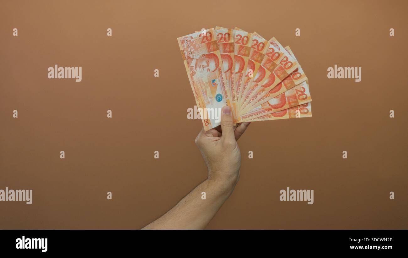 Mano di un uomo caucasico con più pesos filippini su sfondo marrone. Foto Stock
