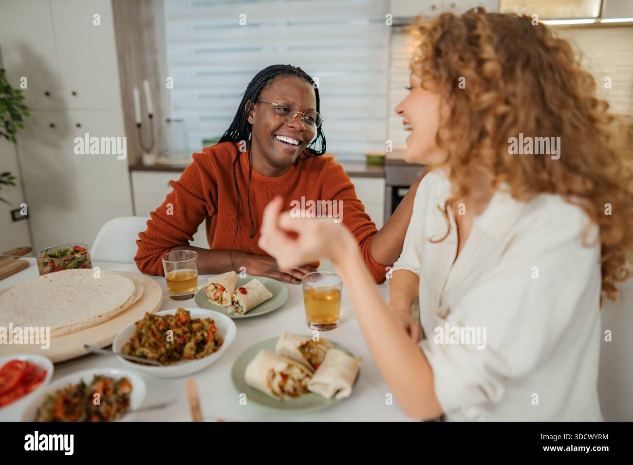 Amici diversi che ridono e pranzano insieme godendo di una conversazione Foto Stock