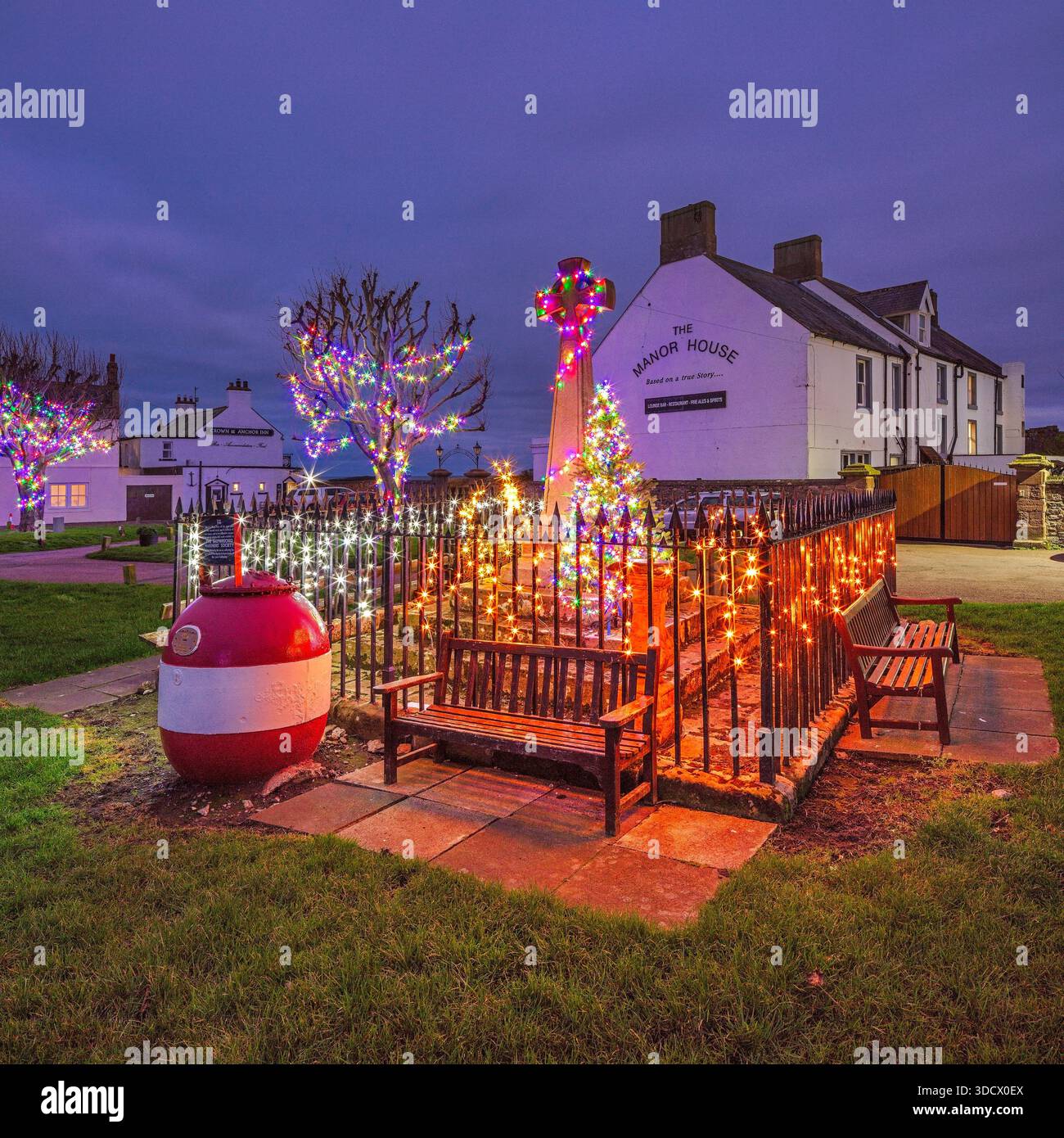Una vista al crepuscolo di Natale dello spettacolo delle luci di Natale nella piazza del villaggio, memoriale di guerra sull'Isola Santa di Lindisfarne nel Northumberland Foto Stock