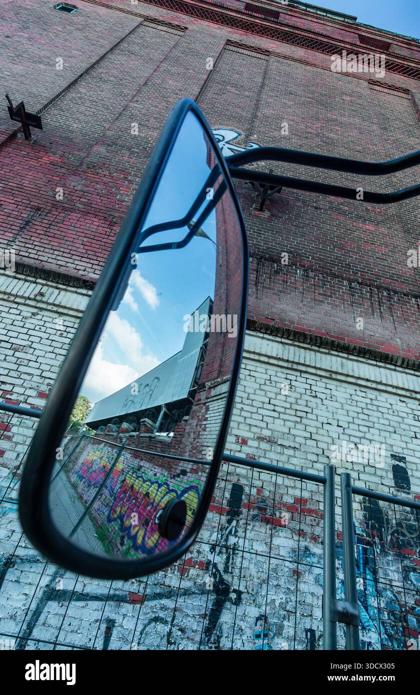 Fotografia artistica grandangolare verticale di un grande specchio a lato dell'autobus montato di fronte a un muro di mattoni in un sito industriale abbandonato a Berlino. Foto Stock