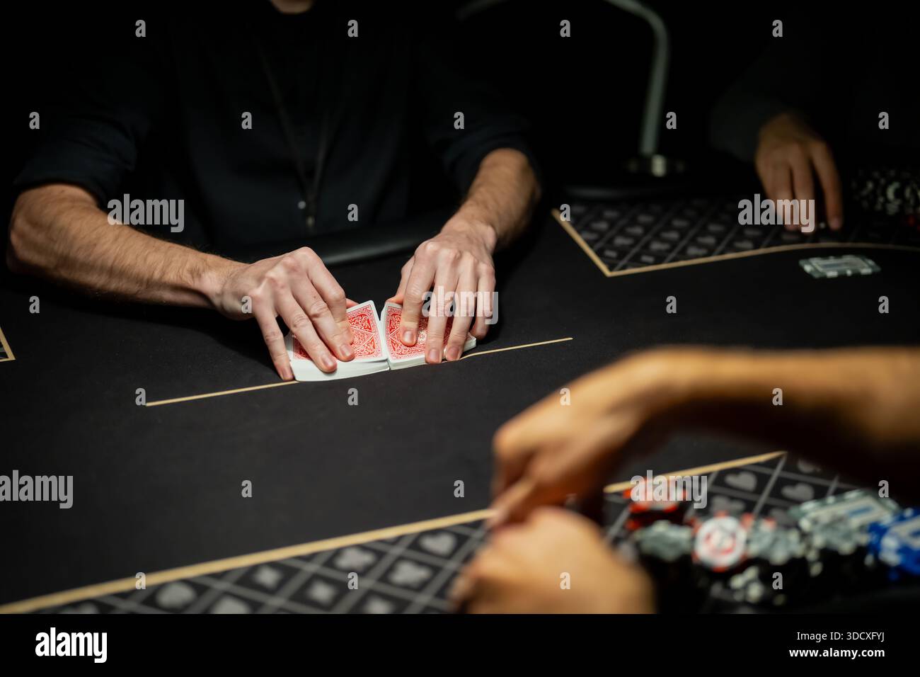 Scena del tavolo da poker del casinò dal vivo con le mani del mazziere che separano il mazzo di carte dalla linea di scommesse mentre i giocatori attendono, mostrando le procedure controllate del settore del gioco Foto Stock
