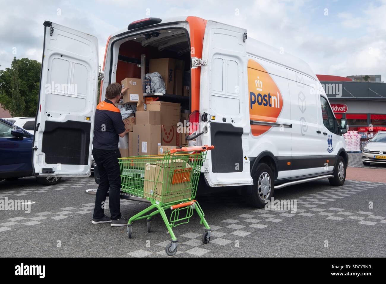 L'autista della società di corriere olandese PostNL scarica i pacchi dal suo furgone e li colloca in un carrello presso un supermercato Foto Stock