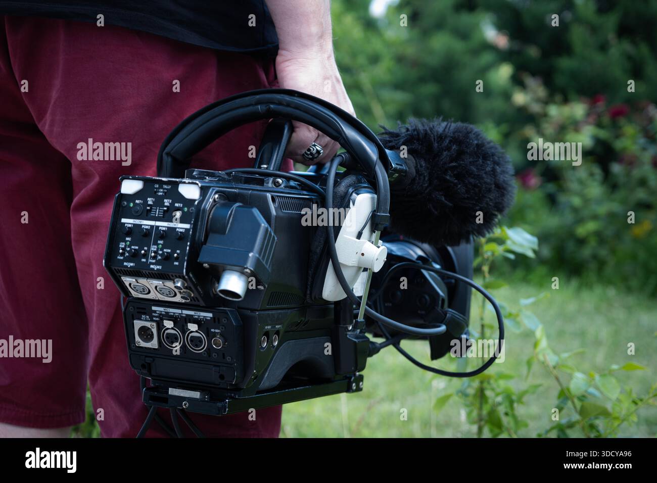 Cameraman che tiene in mano una videocamera professionale per trasmissioni televisive con microfono all'aperto, per catturare filmati per reportage di notizie Foto Stock